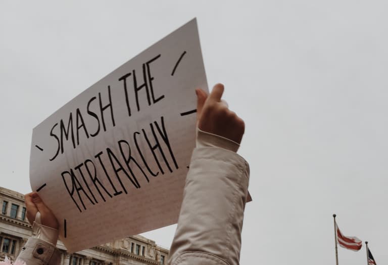 Photo of a person holding a sign “Smash the patriarchy” up in the air during a demonstration